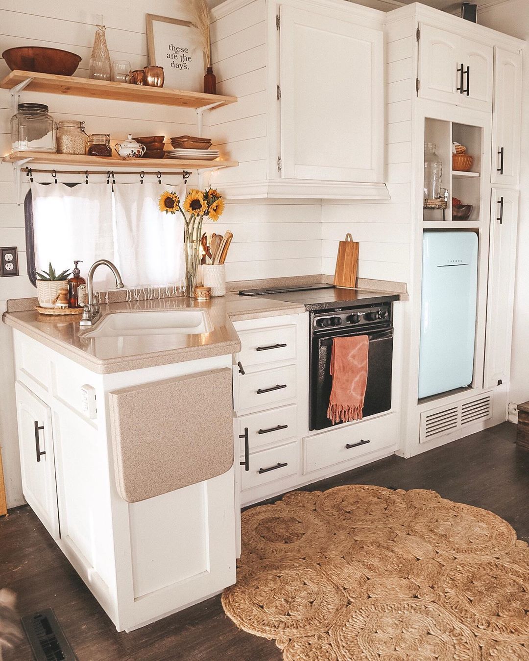 Tiny home kitchen with white cabinets and light blue fridge. Photo by Instagram user @shelbyadrift