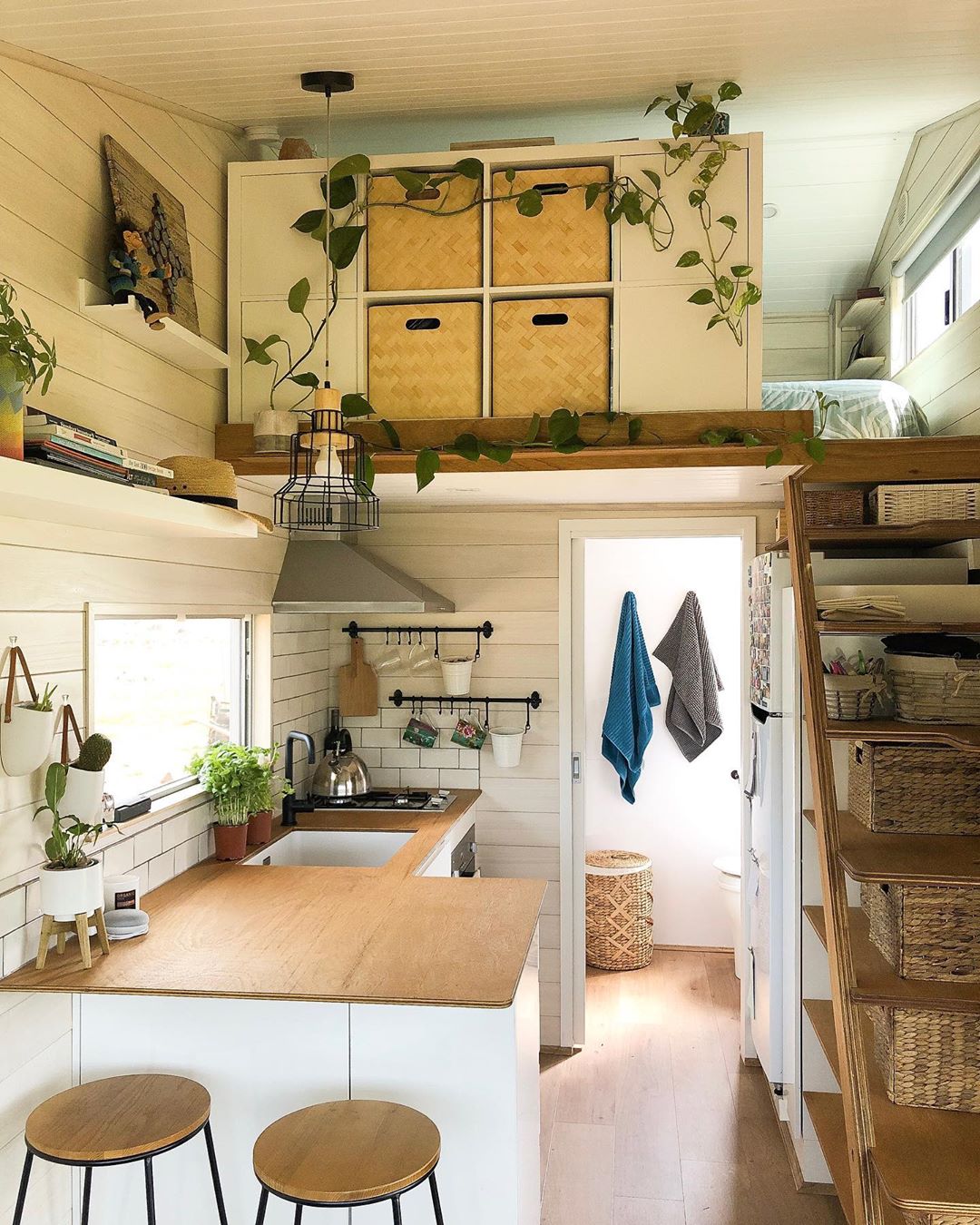 Tiny home with all white walls and plants hanging from ceiling. Photo by Instagram user @girlinatinyhouse