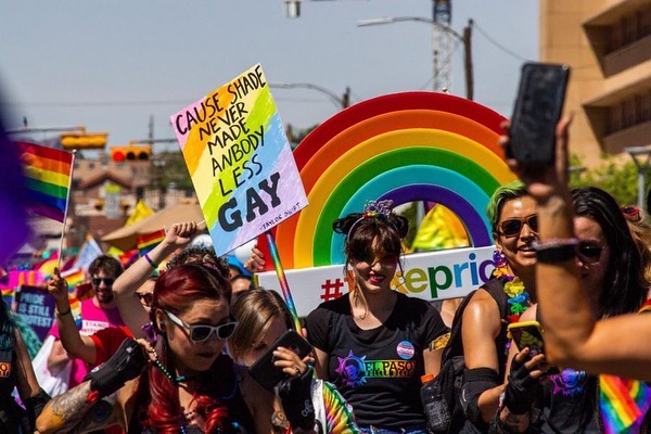 multiple people walking down a street wearing pride color, and signs that suppor the LGBT community. @epsuncitypride