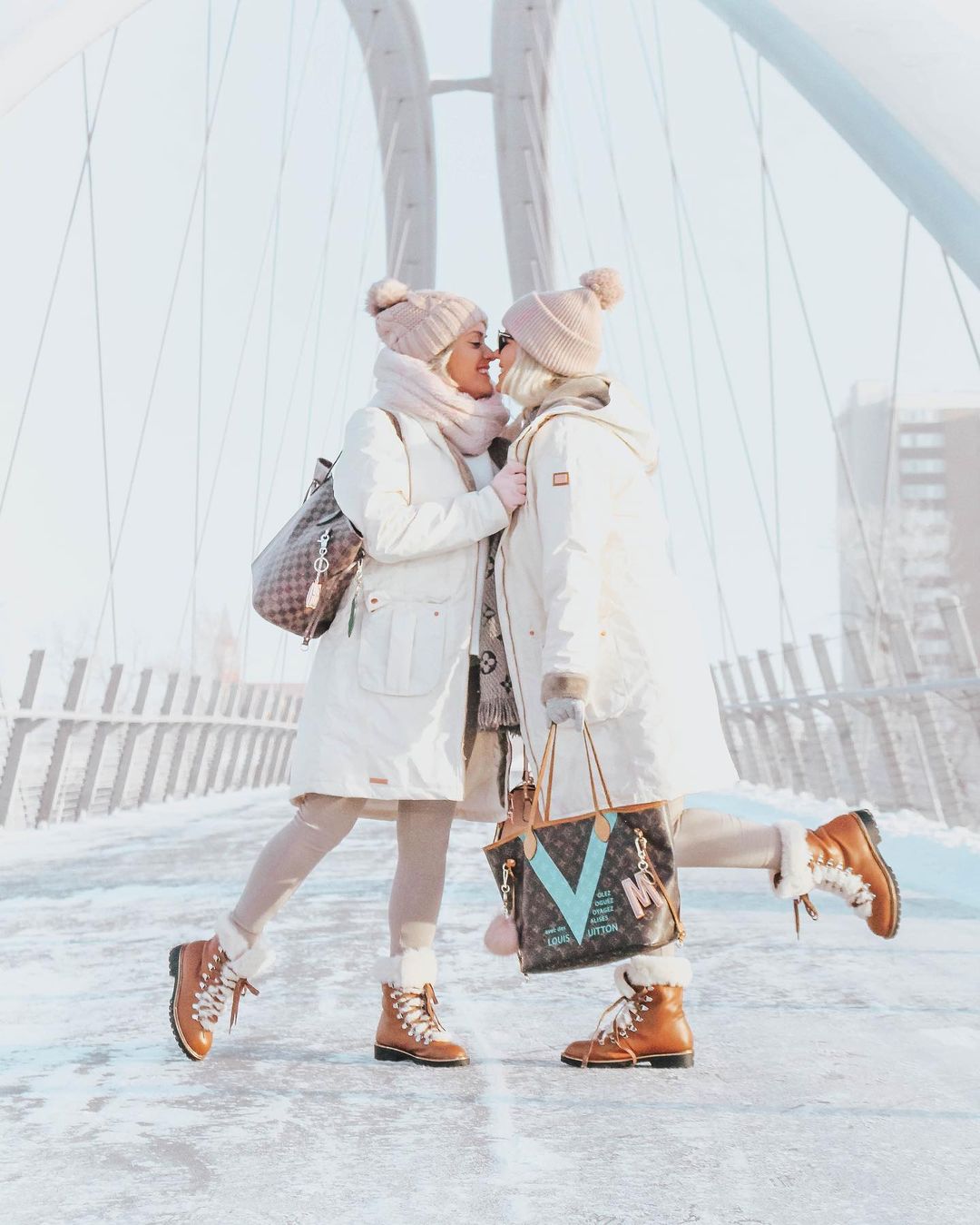 Pictured is two woman embracing each other on a bridge during winter. Photo by Instagram username @whatwegandidnext