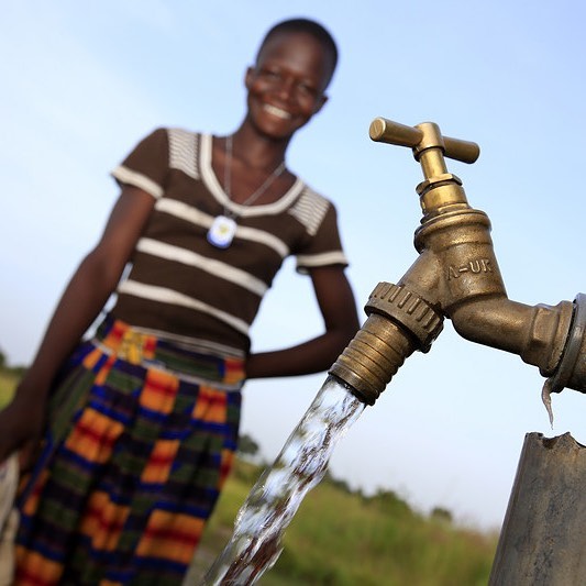 African girl standing by water spout. Photo by Instagram user @oxfamamerica