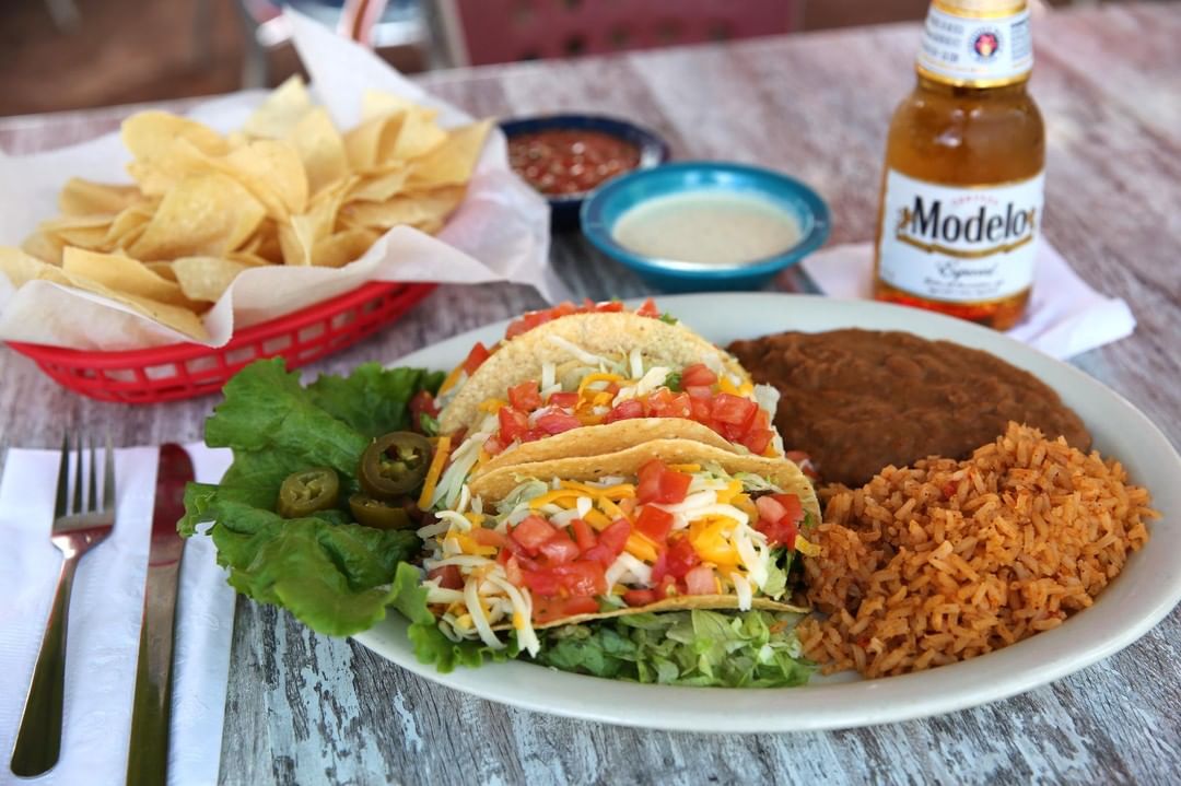 Tacos on a plate next to chips and beer. Photo by Instagram user @chuysrestaurant