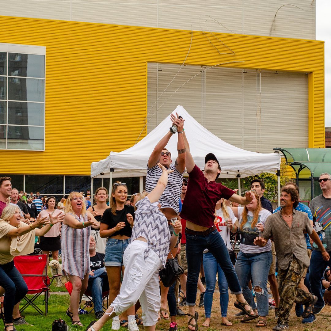 People at the Brew Five Three festival jumping up to catch something in front of a yellow building and white tent. Photo by Instagram user @sip_magazine.