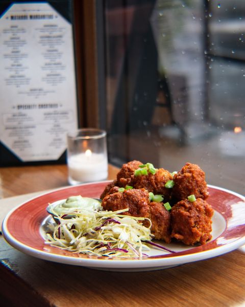 BBQ cauliflower wings on a red plate, with a lit candle beside it and a menu in the background at Matador. Photo by Instagram user @matador_restaurants.