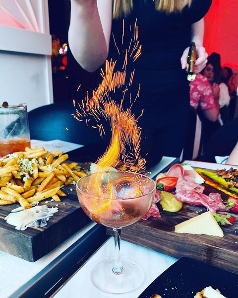 A bartender setting a drink on fire in front of plates of fries and charcuterie at The Boom Boom Room Tacoma. Photo by Instagram user @food_flexin.