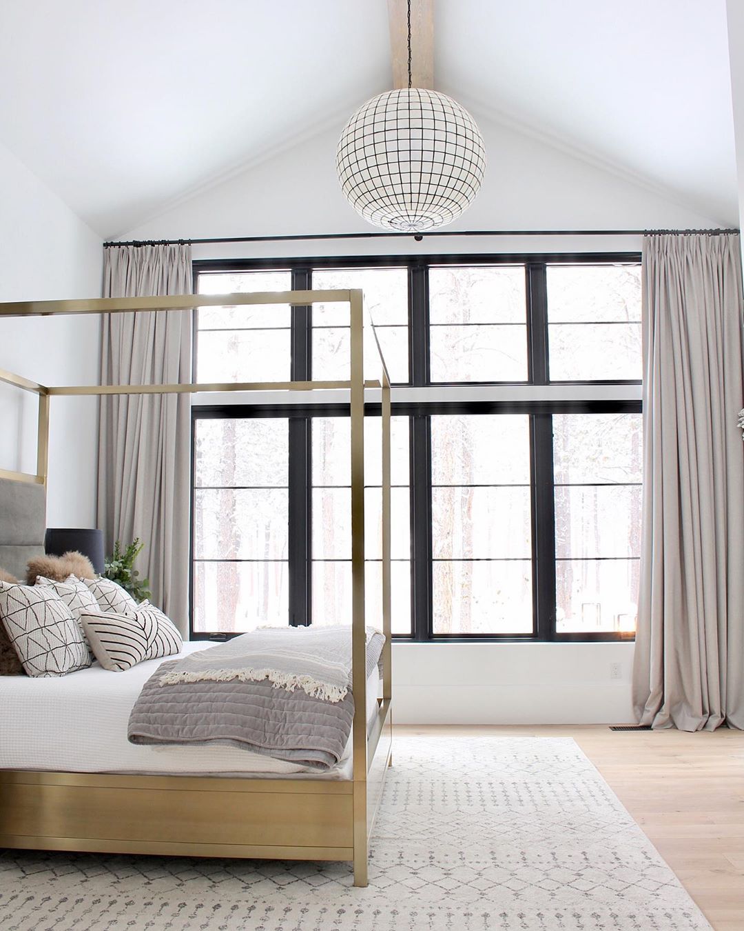 White bedroom with tan window curtains and gold four-post bed. Photo by Instagram use @thehouseofsilverlining