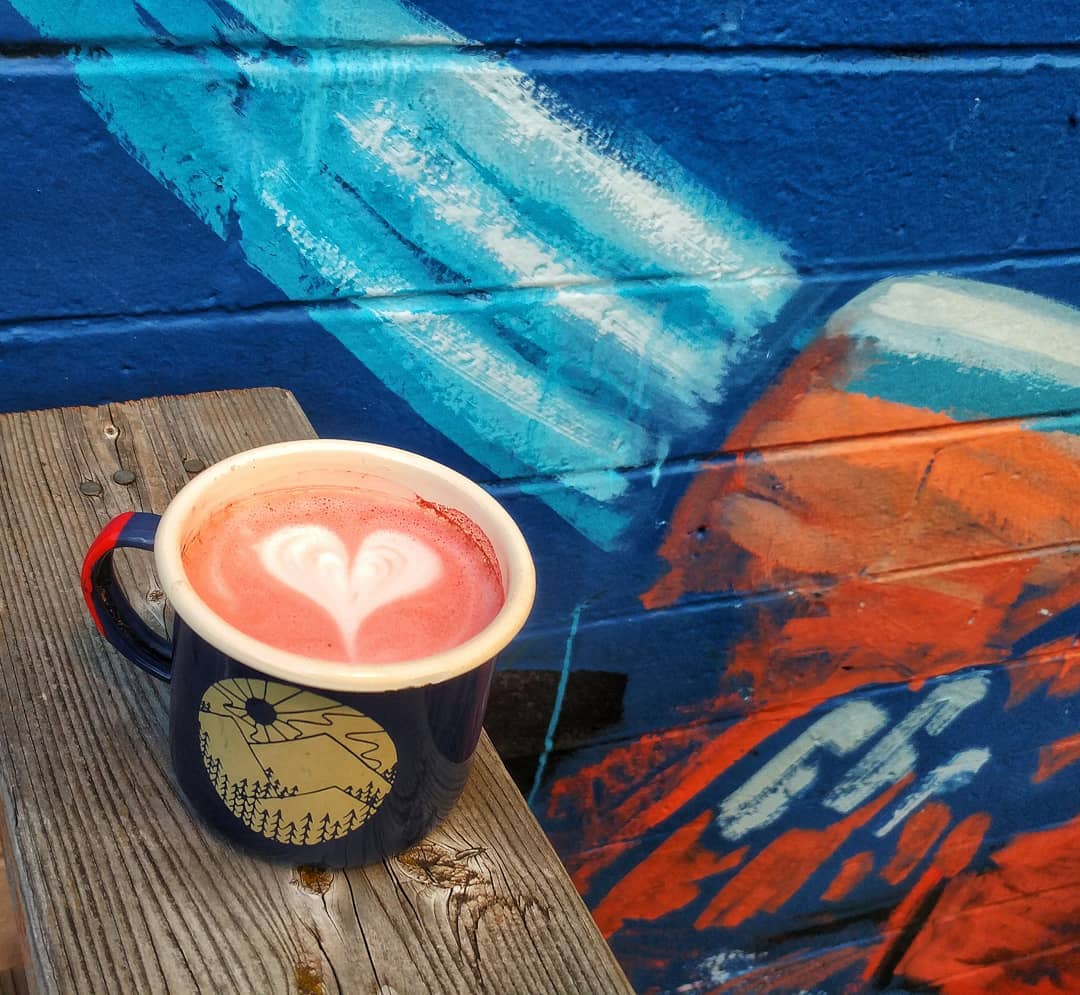 Coffee cup with heart latte art by blue wall. Photo by Instagram user @cosmonautcoffee