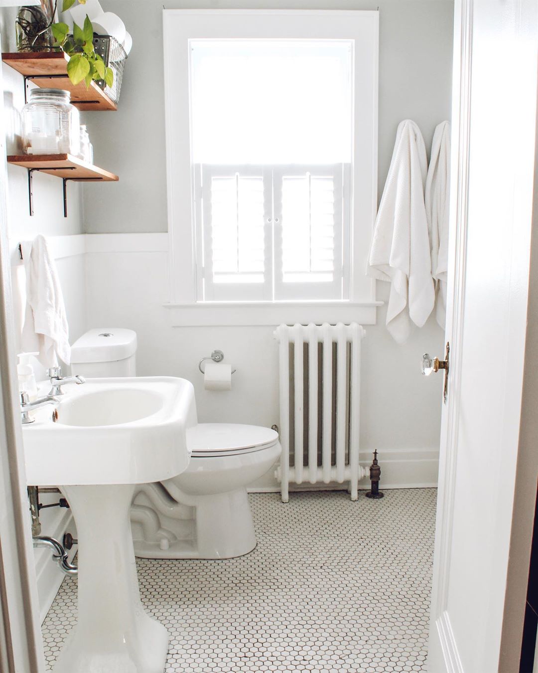Small, all-white bathroom with wood shelves. Photo by Instagram user @thelittlebylittlehome_