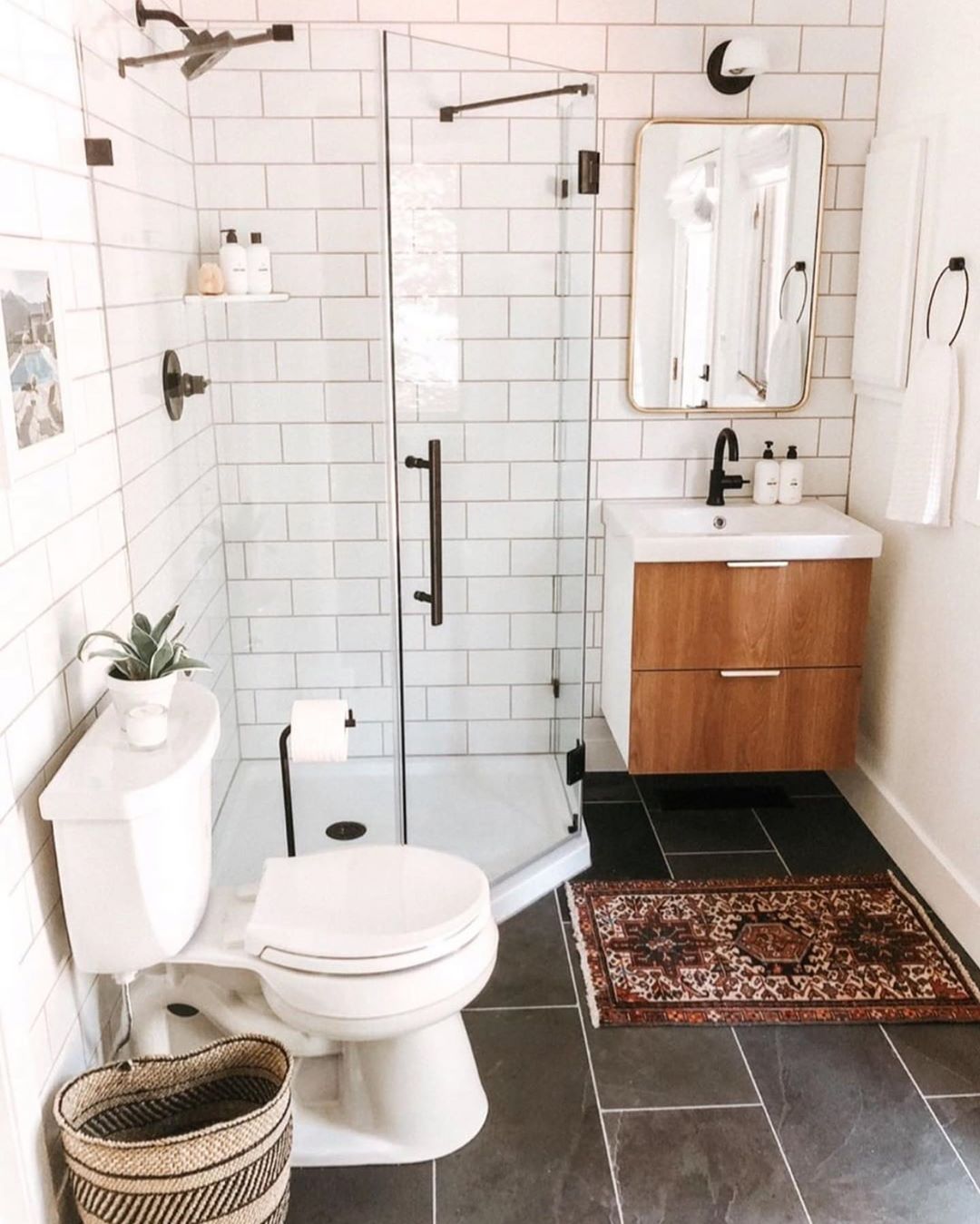 Small bathroom with white wall tile and dark floors with glass shower. Photo by Instagram user @kyrosdesigns