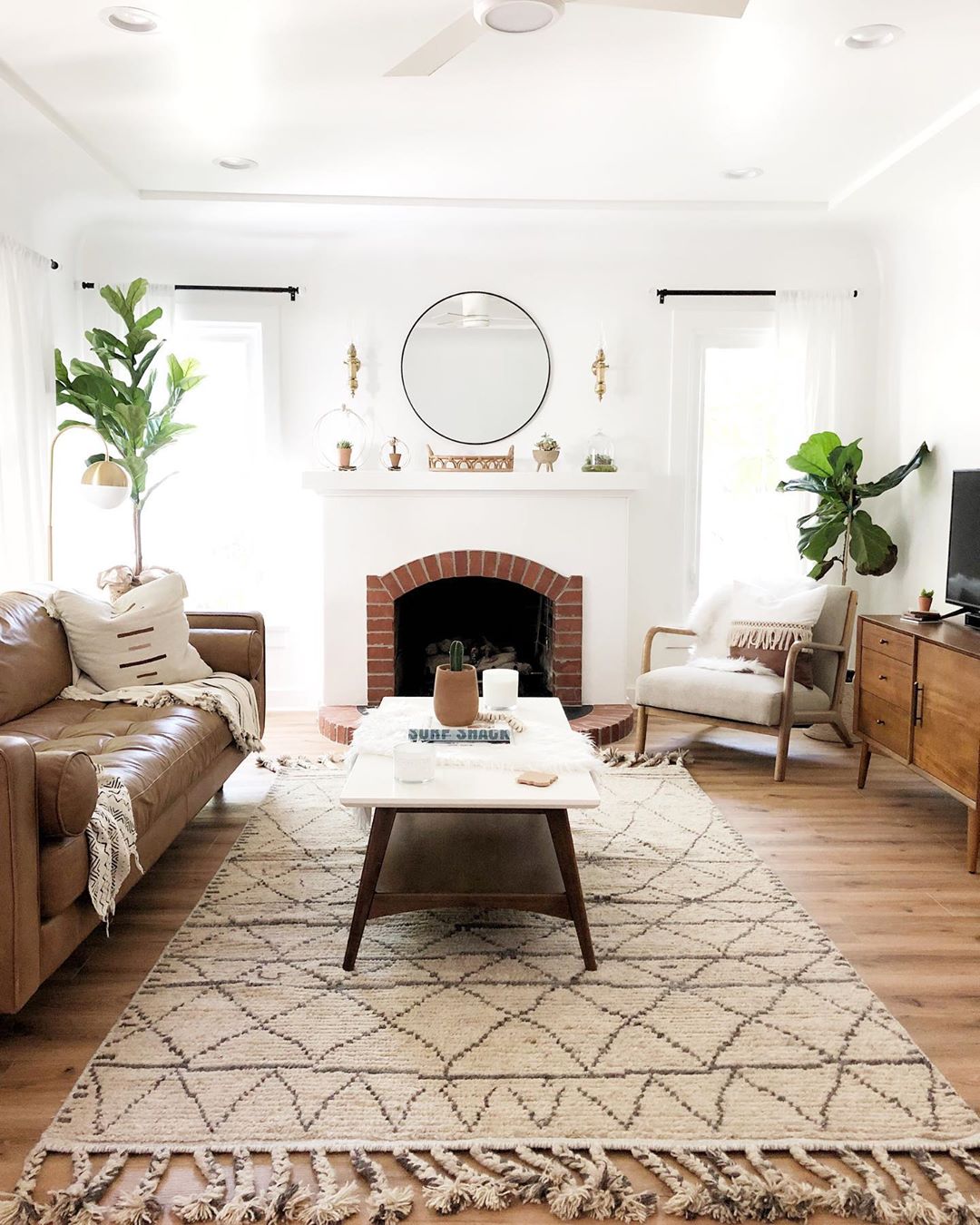 White-painted living room with wood floors and brown leather couch. Photo by Instagram user @cottageandsea