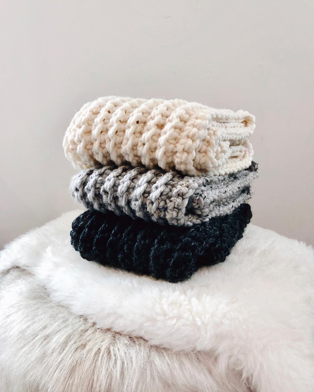 Scarves folded on white fur pillow. Photo by Instagram user @eikachickaknits