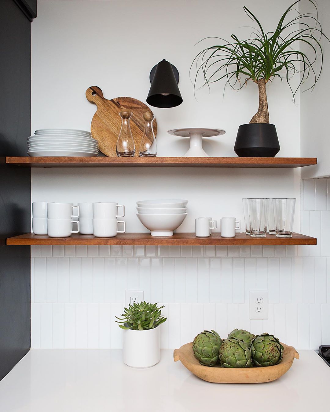 Dark wood floating shelves with white dishes on them. Photo by Instagram user @adidstudio