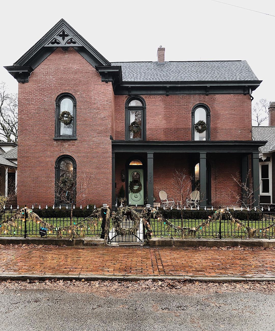 Two-story red brick house with black trim and wrought iron fence. Photo by Instagram user @hollyvioletragsdale