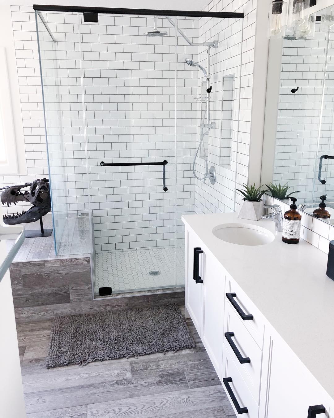 White-tile bathroom with wood floors and glass shower. Photo by Instagram user @kling_designs