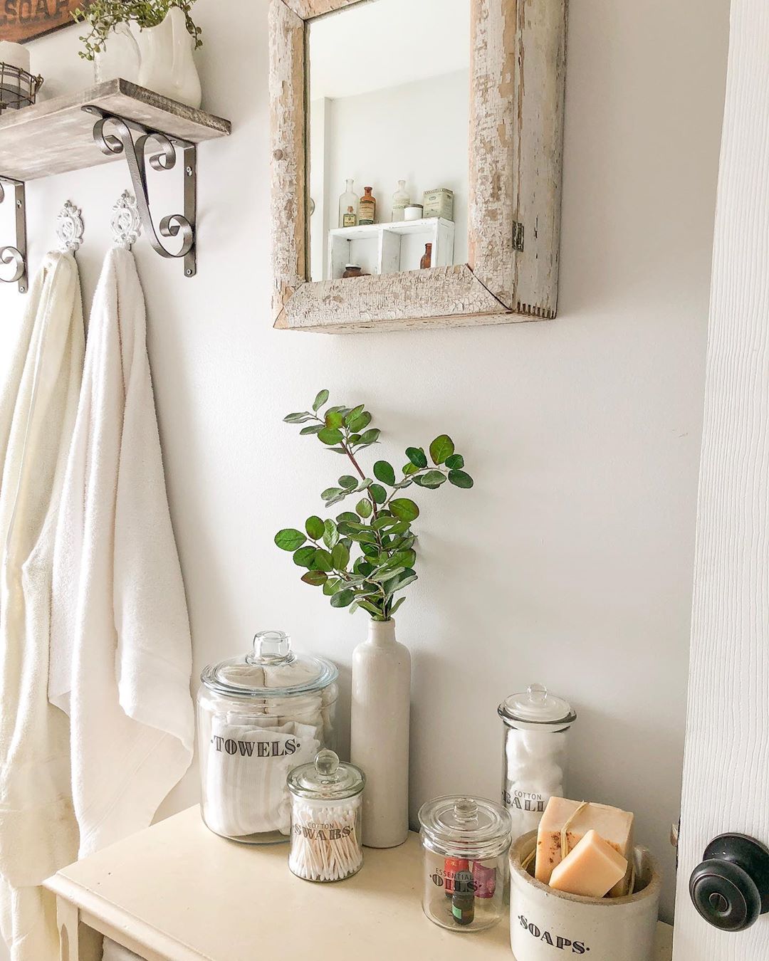 White cabinet with glass jars and rustic mirror hung above cabinet. Photo by Instagram user @the.huber.homestead