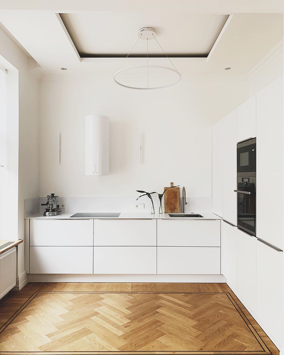 Minimalist kitchen with white walls, white cabinets, and wood floors. Photo by Instagram user @thneu