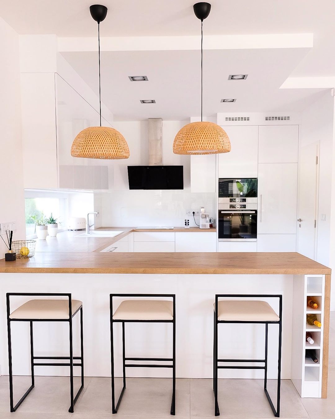 All-white kitchen with wood countertops and yellow light fixtures. Photo by Instagram user @morhome_hun
