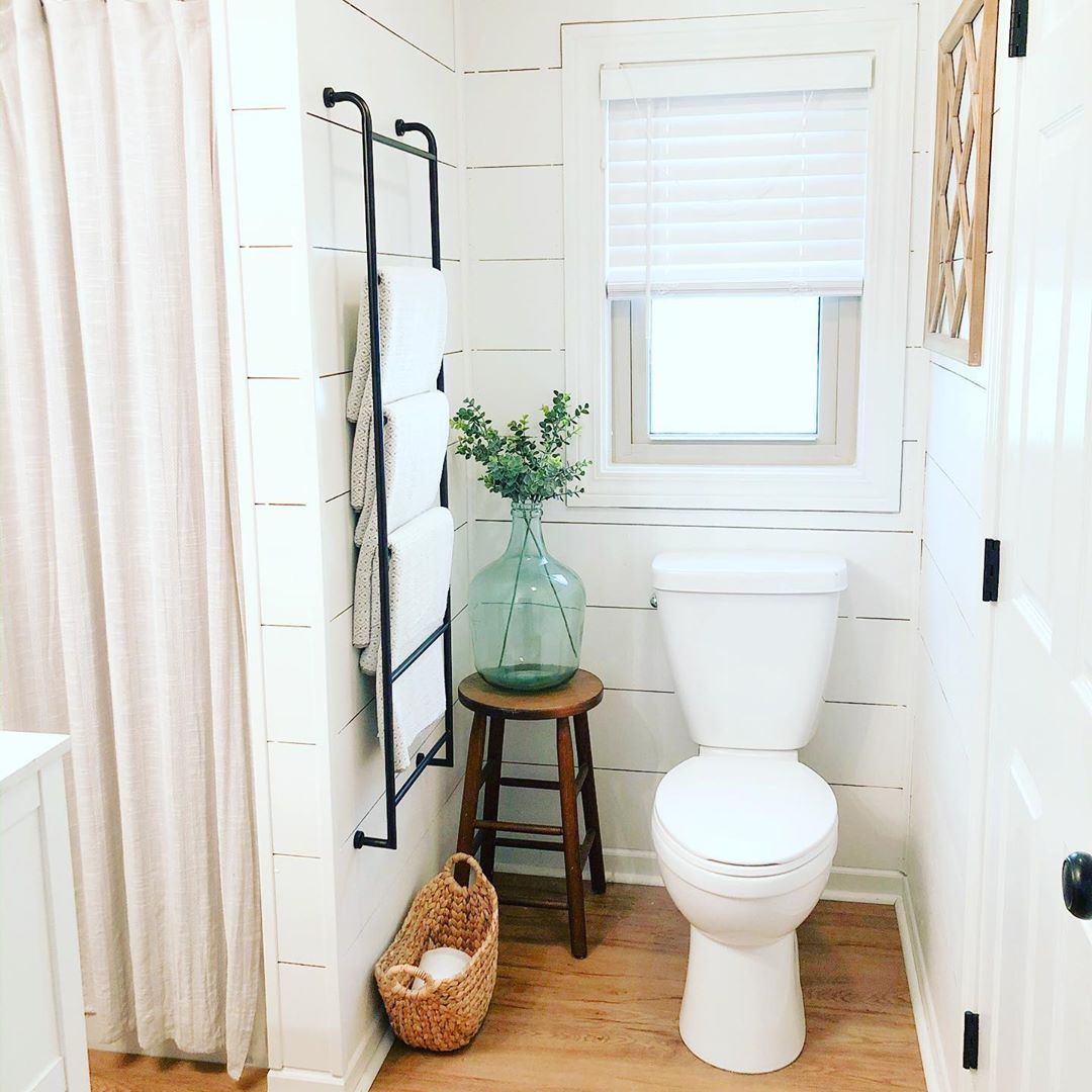 White bathroom with wood floors and vase on stool by toilet. Photo by Instagram user @tinycottageonpetes