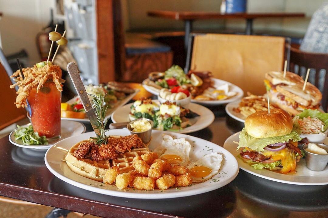 Plate of waffles, eggs, and tater tots by cocktail. Photo by Instagram user @bay_local