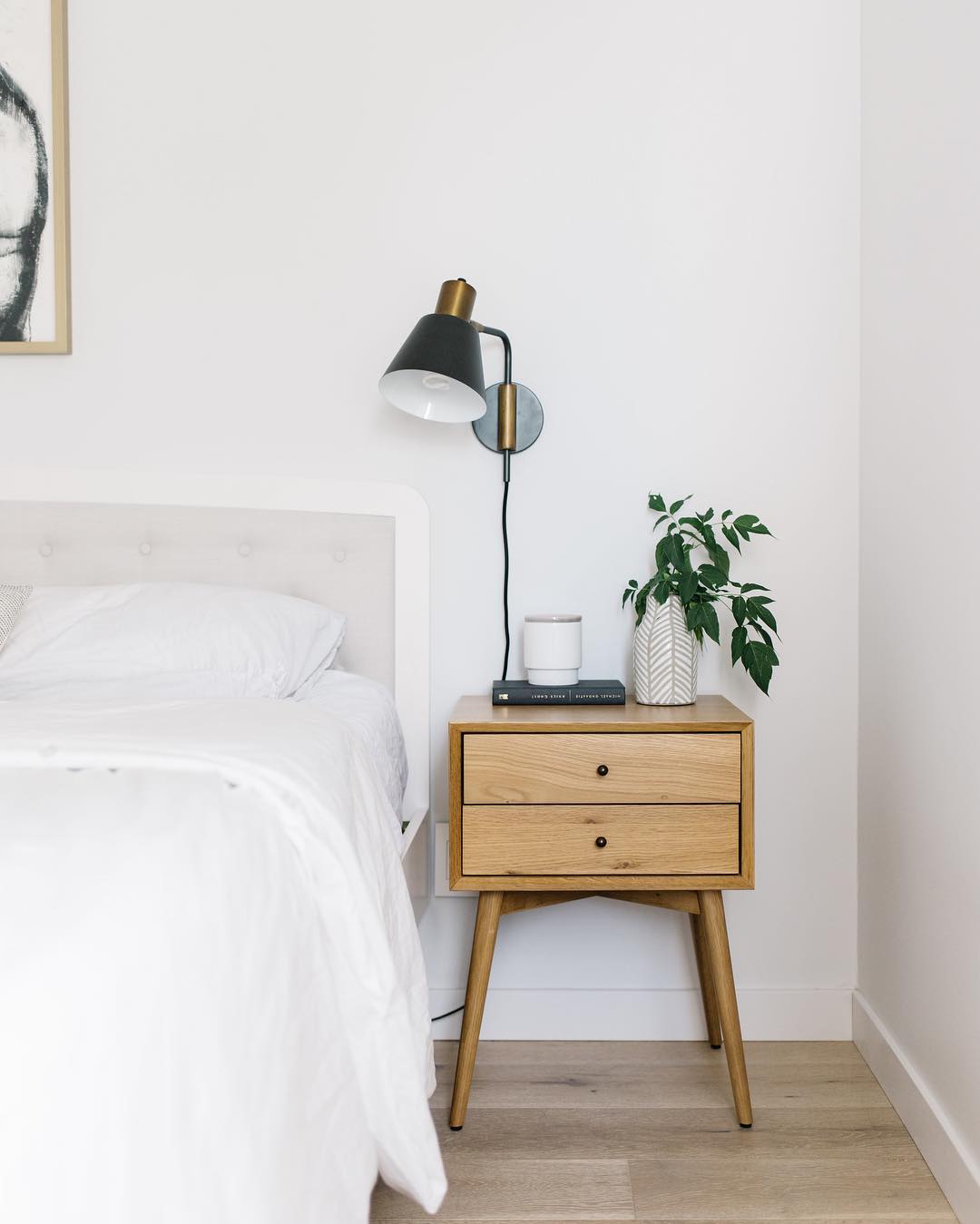 White bedroom with brown nightstand and white bed. Photo by Instagram user @bykristinalynne