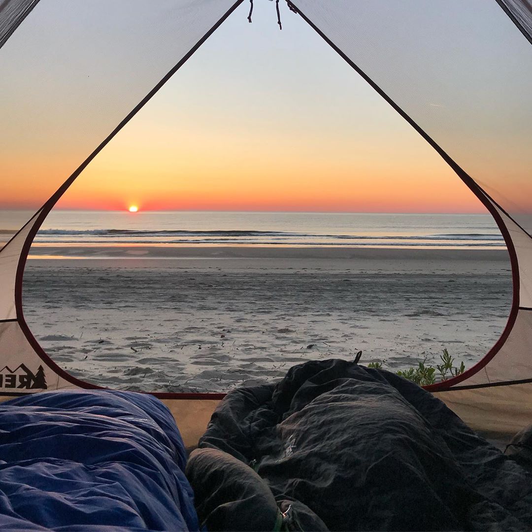 Tent sitting on beach facing the ocean at sunset. Photo by Instagram user @our.weekend.adventures