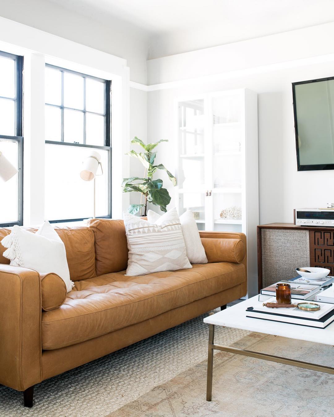 Tan leather couch in front of big window in all-white living room. Photo by Instagram user @nicoledianne
