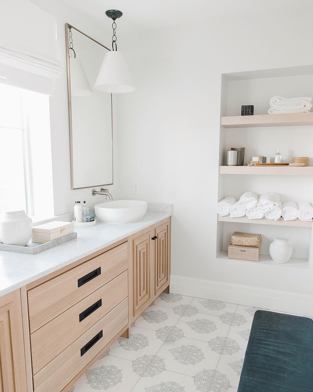 All-white bathroom with blue rug and wood vanity. Photo by Instagram user @kristinabills