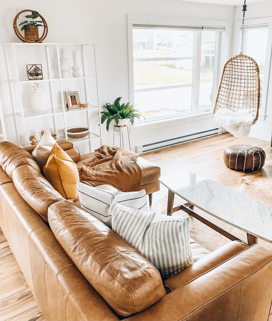 White-painted living room with tan leather couch and chair hung in corner. Photo by Instagram user @boneill_athome