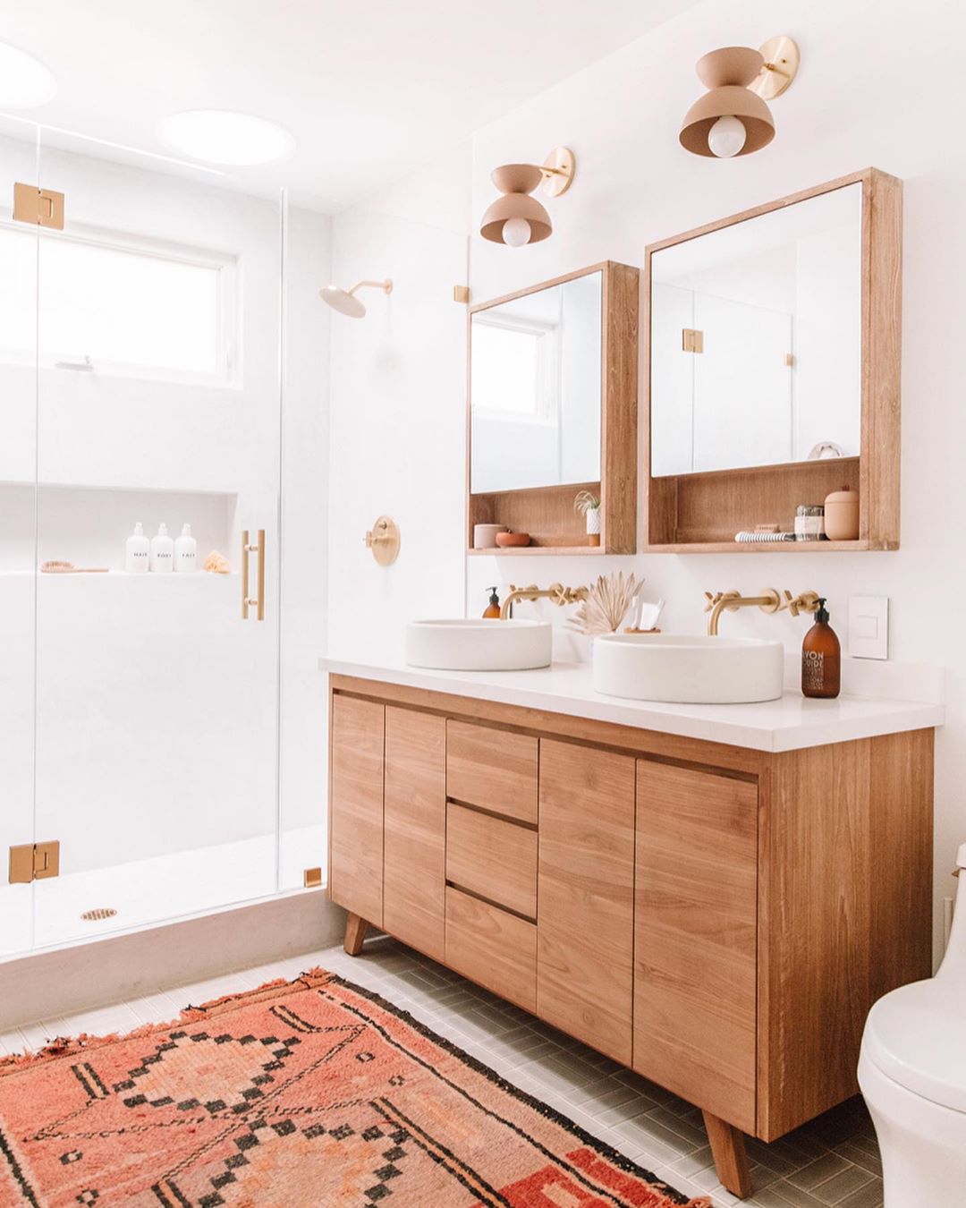 White bathroom with wood cabinet and orange rug. Photo by Instagram user @jeffmindell