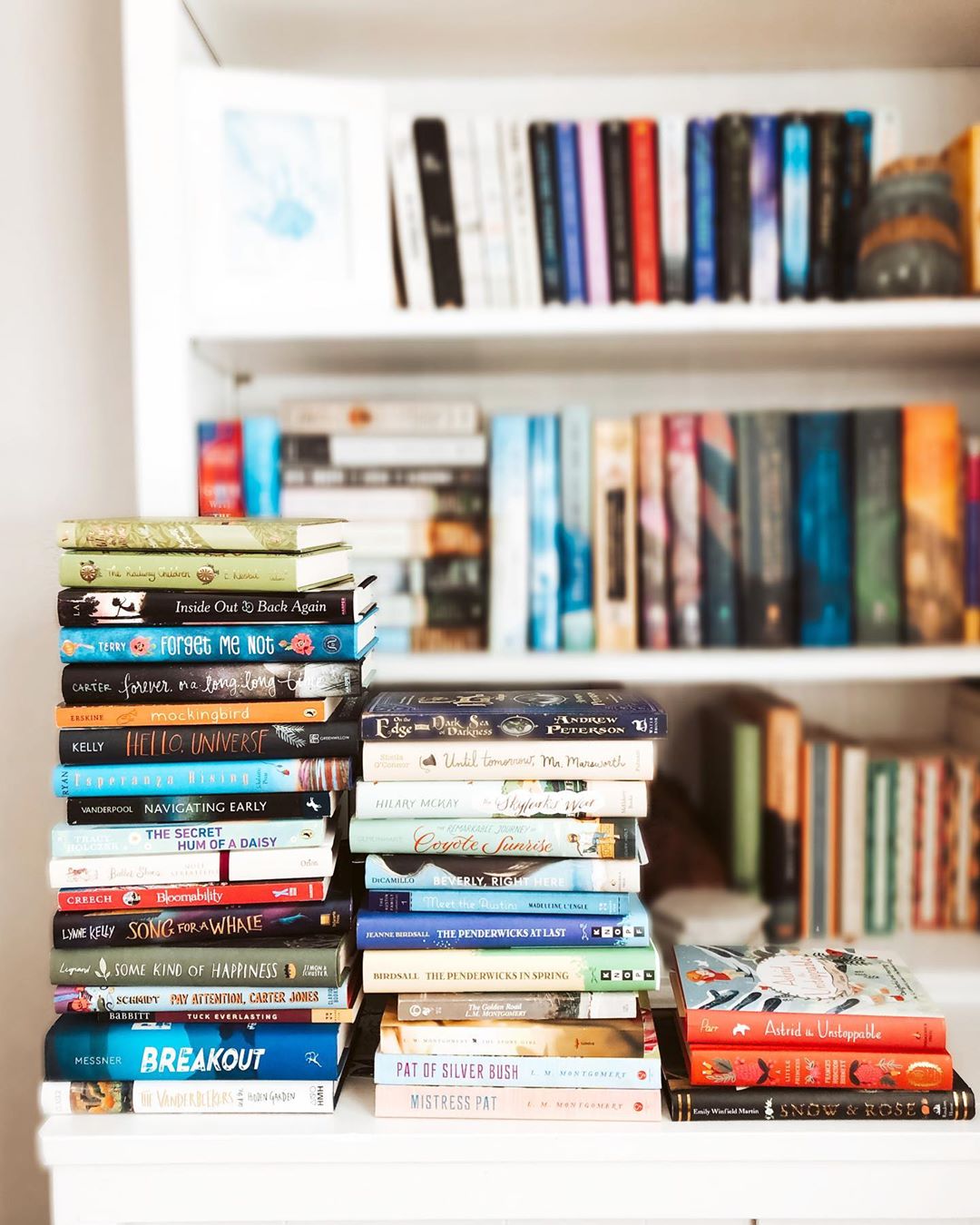 Books stacked by a bookshelf. Photo by Instagram user @lifebetweenwords