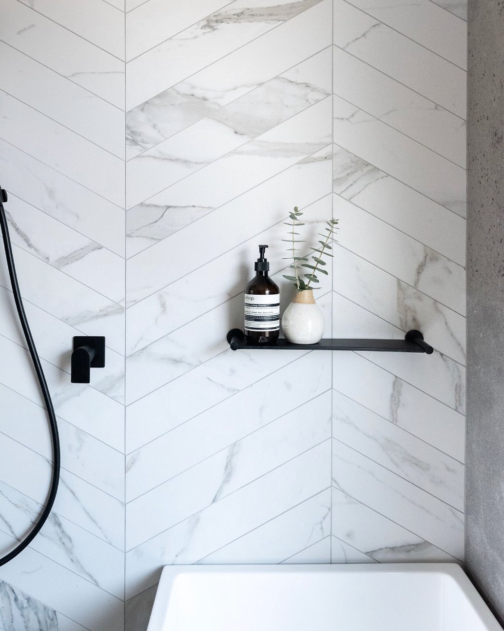 Marble tile bathroom with black floating shelf about tub. Photo by Instagram user @hatchrenovations