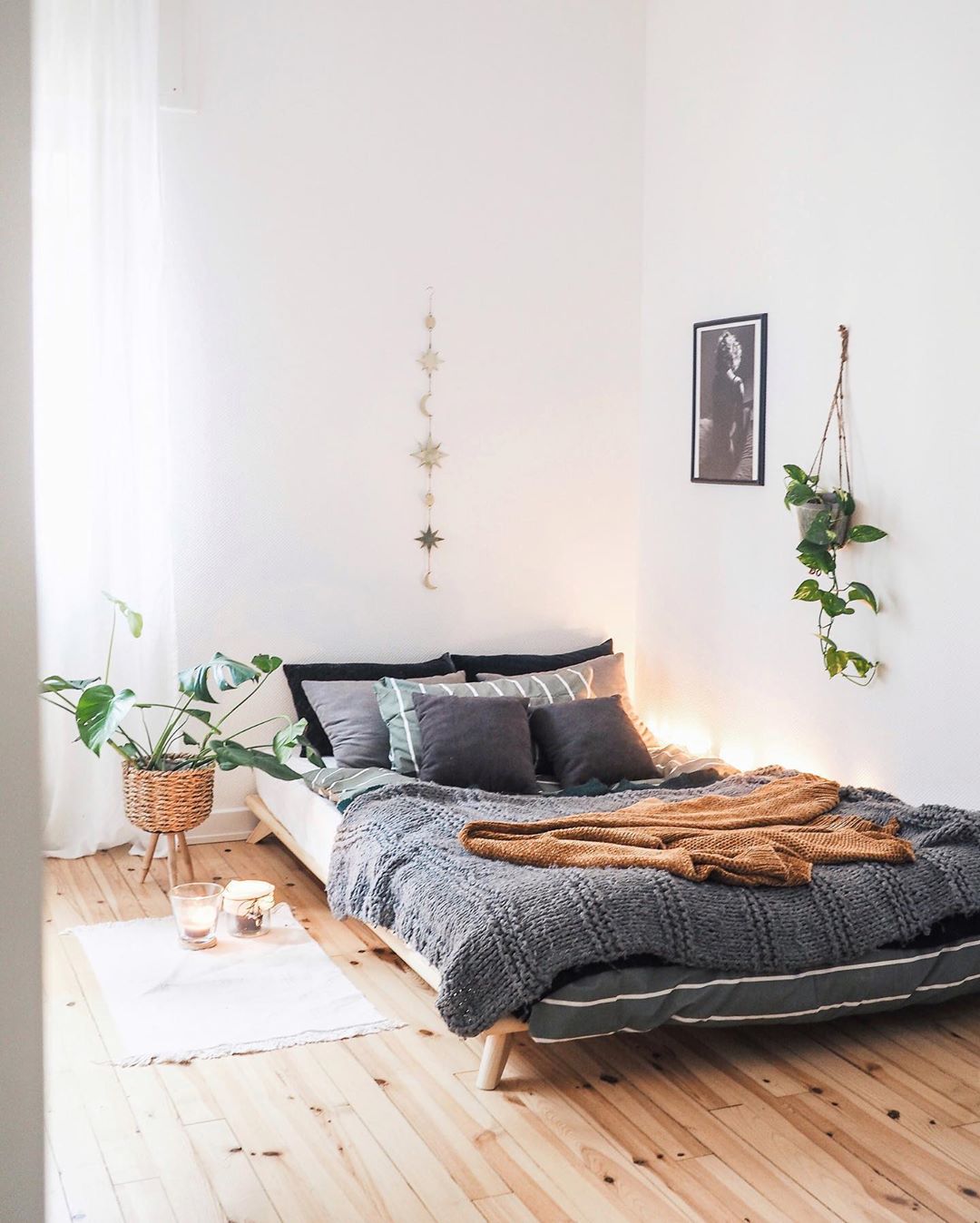 White bedroom with gray bed, plants, and wood floors. Photo by Instagram user @what.the.hygge