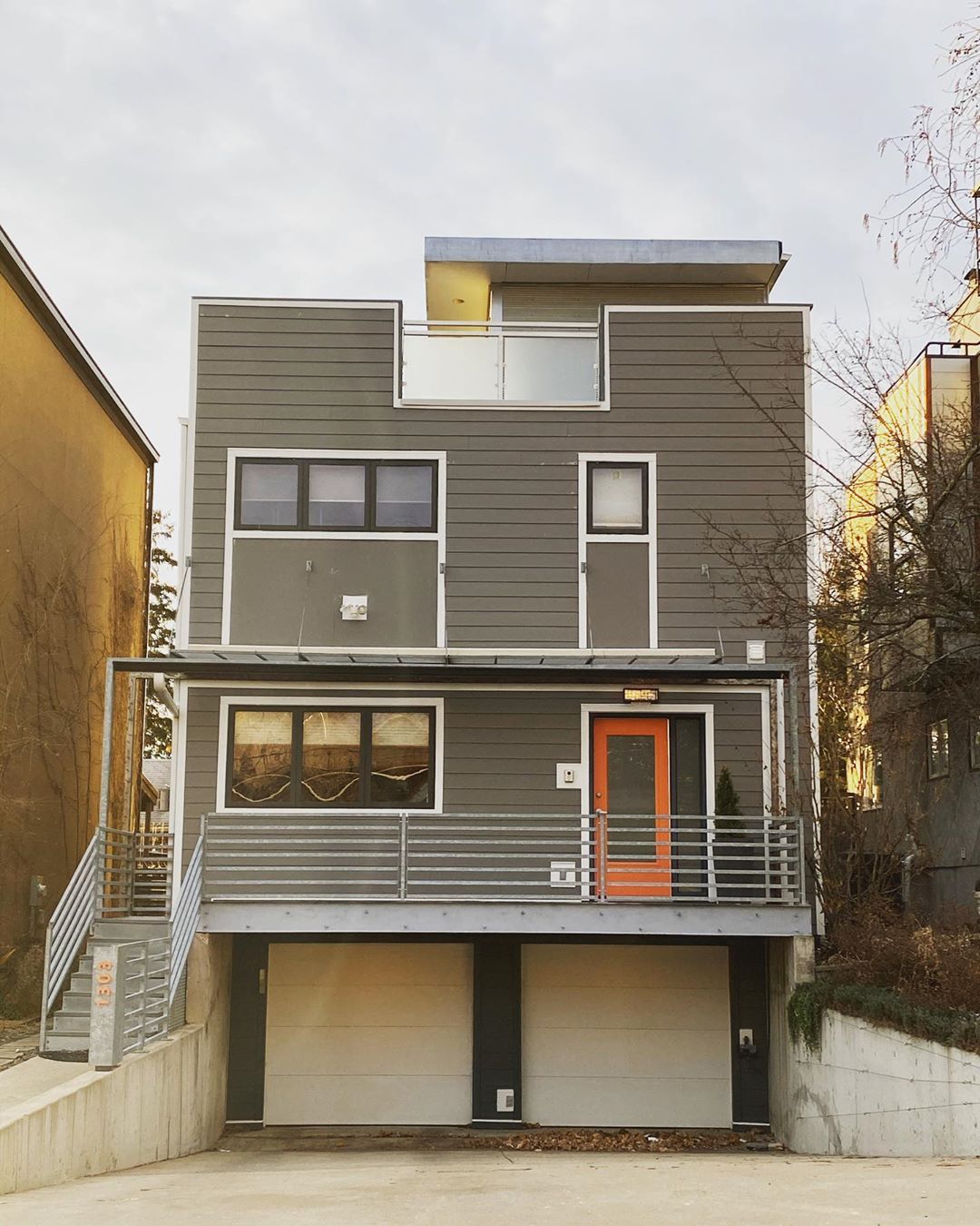 Two-story modern gray home with orange door. Photo by Instagram user @discoverkc