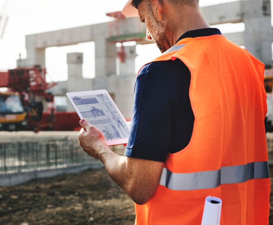 Man wearing orange construction vest looking at paper. Photo by Instagram user @osuit