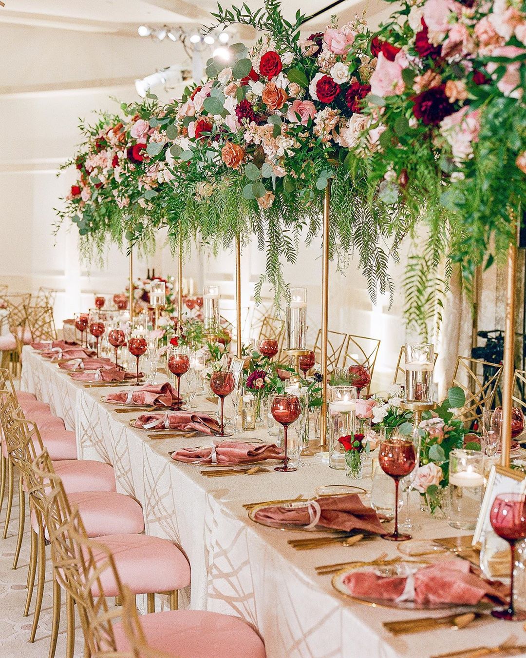 Table with pink chairs and centerpieces of bright red flowers. Photo by Instagram user @alexwphotography