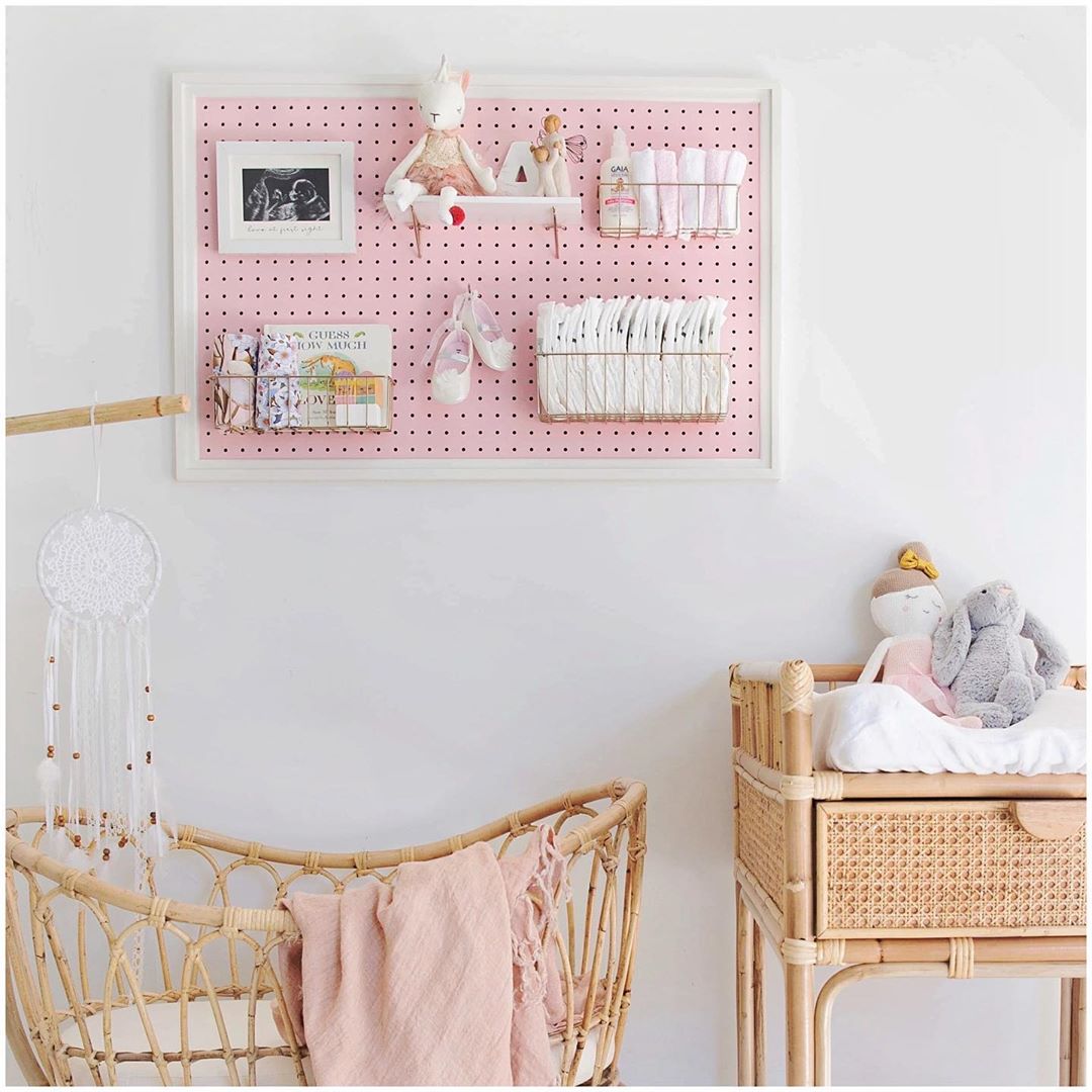 pink homemade pegboard with items stuck to it and wooden bassinet photo by Instagram user @pinpegandhome