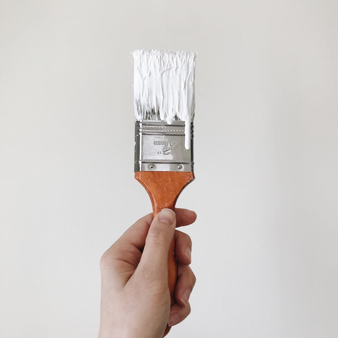 Hand holding paint brush with white paint. Photo by Instagram user @nikkihofmeister