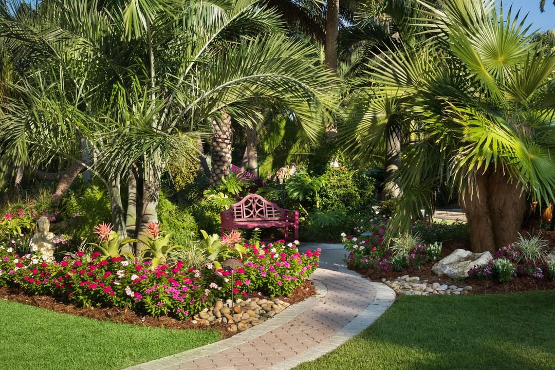 backyard landscaping with large trees and colorful planters with a paved pathway leading to a bench photo by Instagram user @rswalsh