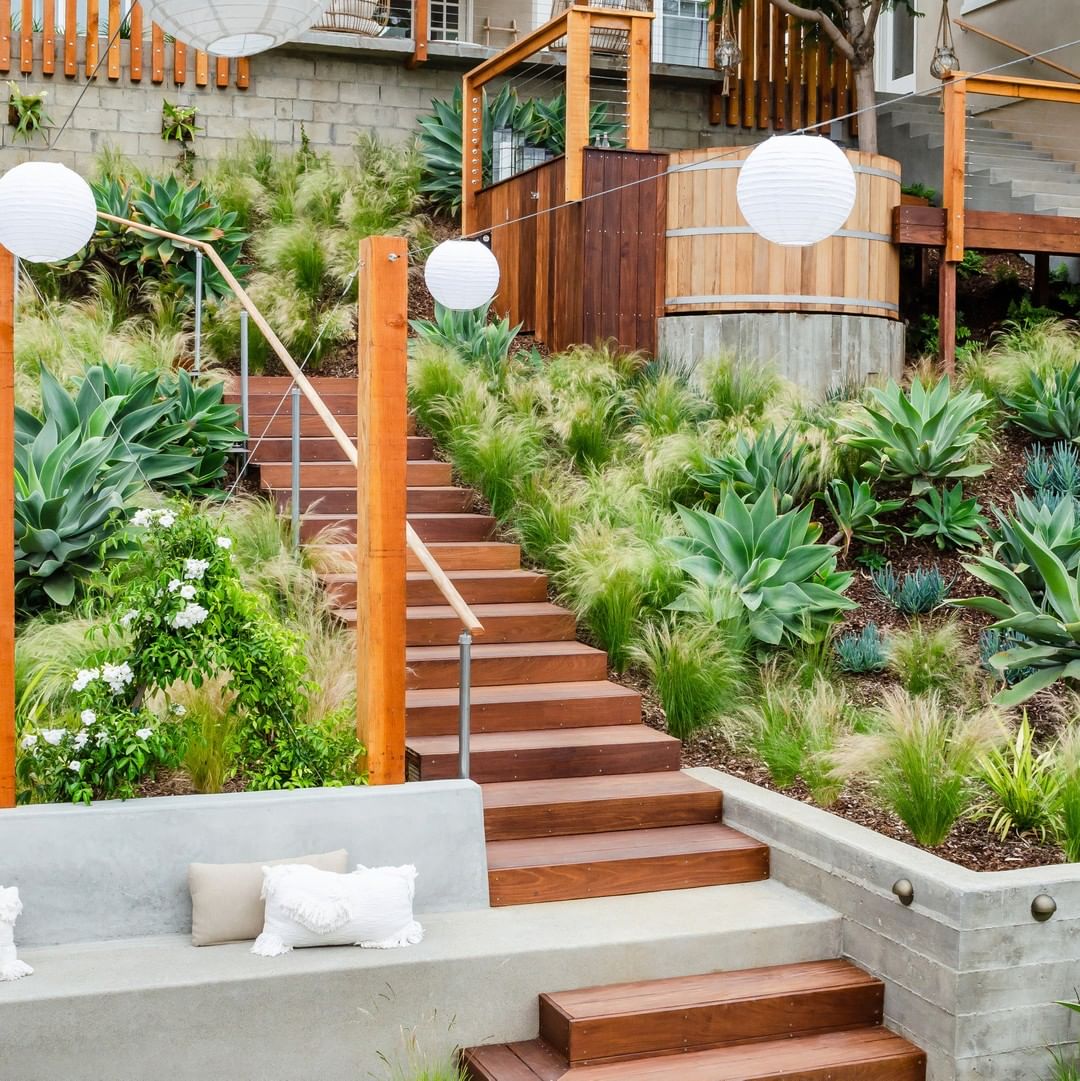 backyard landscaping with wooden stairs and native plants surrounding a small sitting area with lanterns strung above photo by Instagram user @brookside_design