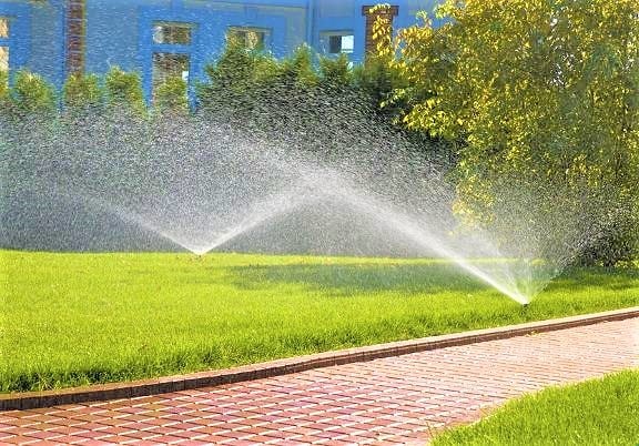 sprinklers watering a healthy lawn with wet brick walkway photo by Instagram user @saddlerivermagazine