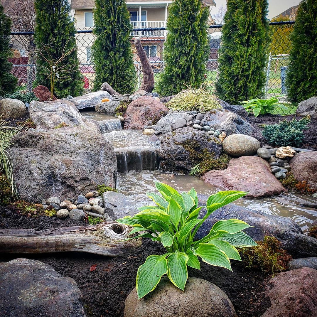 outdoor waterfall built into backyard landscaping photo by Instagram user @fontanawaterfeatures