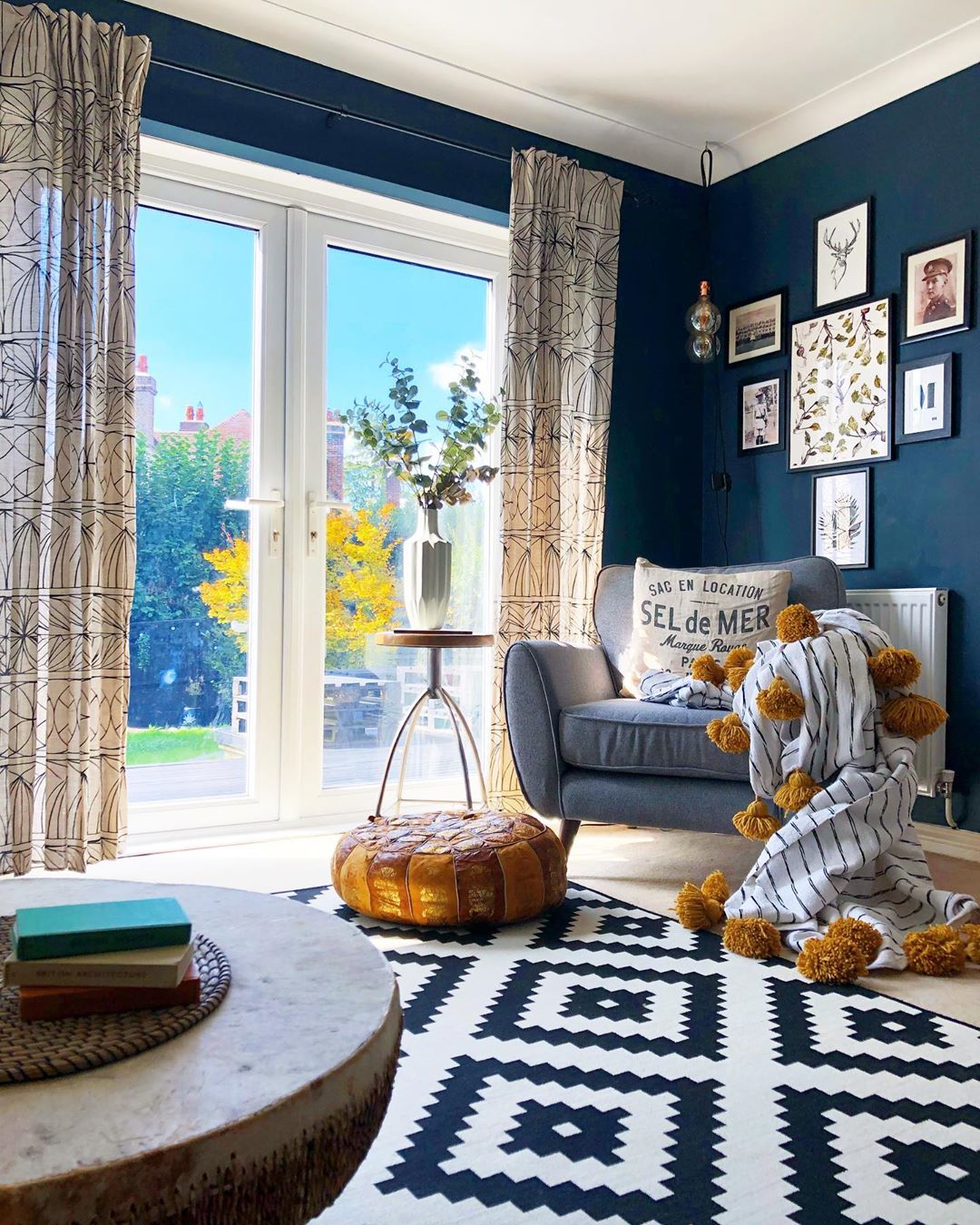 living room with blue walls and white and blue area rug with lots of natural light photo by Instagram user @nest_twenty_eight