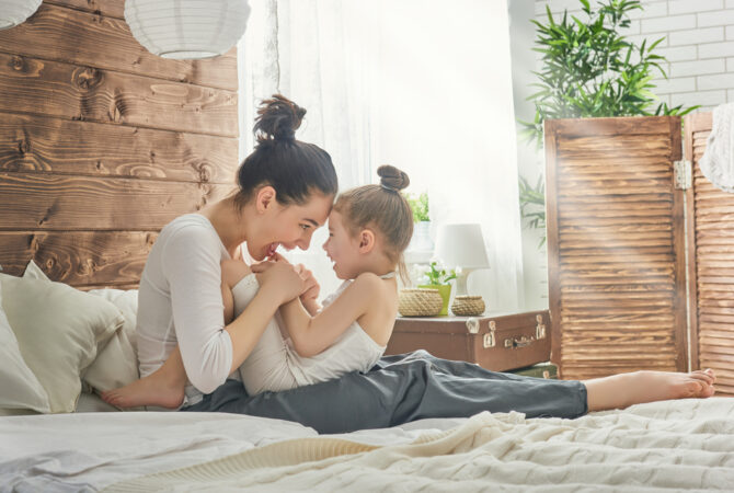 Mom and young daughter playing on bed