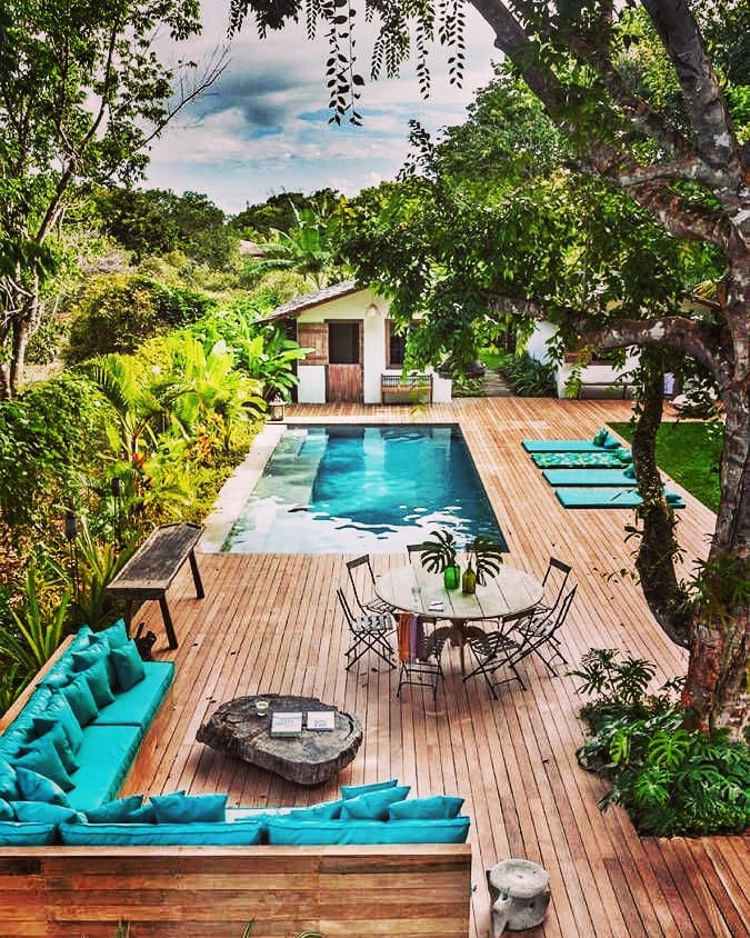 large backyard patio with l-shaped couch and pool along wooden patio photo by Instagram user @decoracionpatiosyjardines