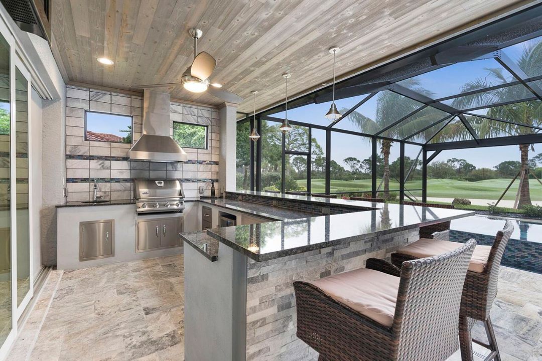 outdoor kitchen with large counter and pool under a lanai photo by Instagram user @grandeconstructionfl