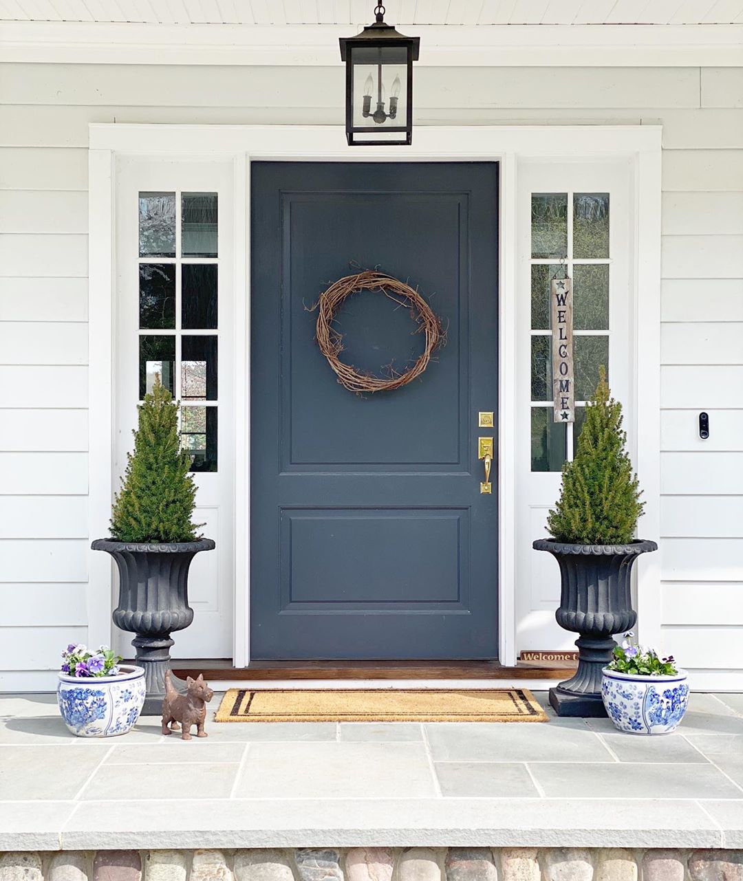 front door that has been painted a slate blue with decorative wreath hanging on it photo by Instagram user @chrissiehomeanddesign
