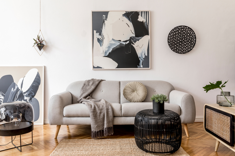 A living room with a gray couch in front of a white wall with black and white decorations