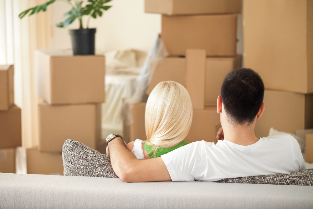 man and woman sitting on a couch in front of cardboard boxes