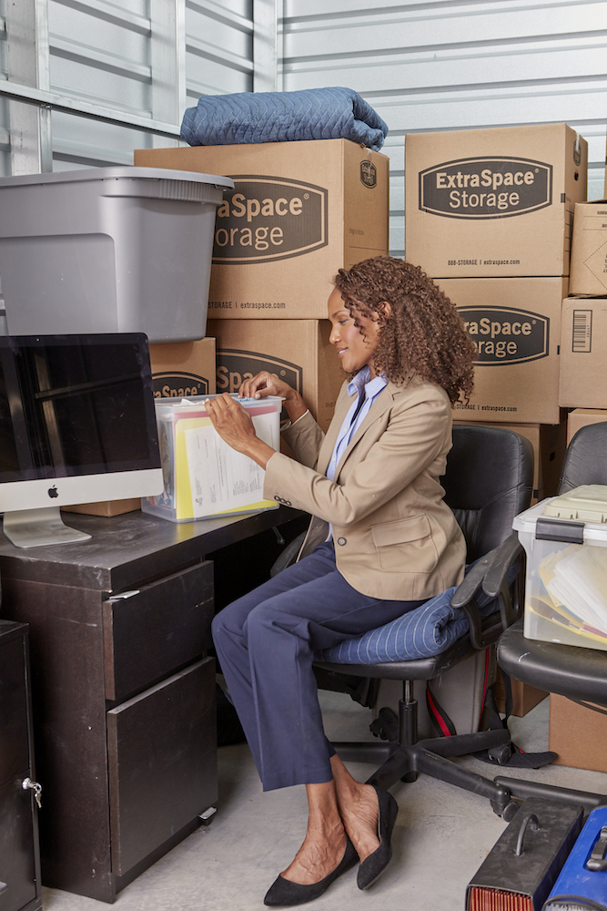 Woman Sitting at a Desk in a Small Storage Unit with Extra Space Storage Boxes Around Her