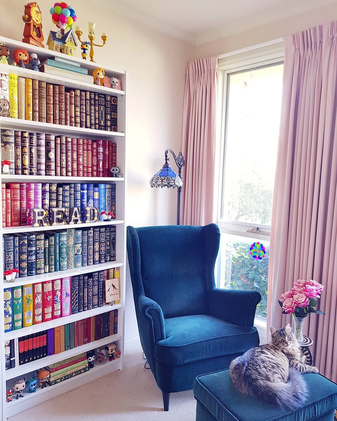 Reading Area with a Blue Chair and a Tall Bookcase Organized by Color. Photo by Instagram user @enchanted_bookshelf